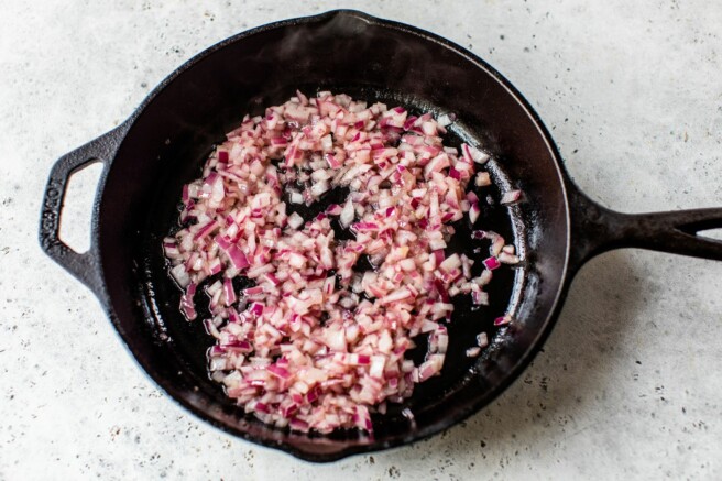 Sautéing diced red onion in a large cast iron skillet.