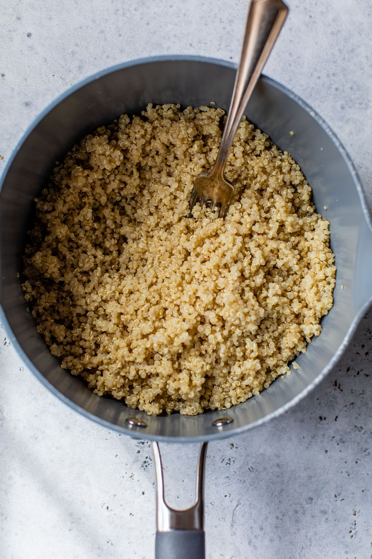 Fluffing quinoa with a fork in a large saucepan.