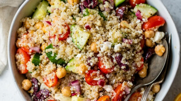 Greek quinoa salad served in a white bowl with a spoon and fork.