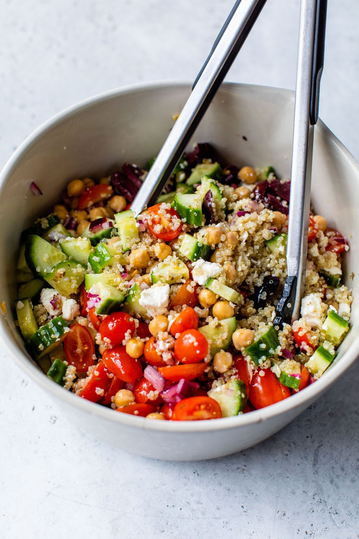 Tossing together veggies with quinoa and dressing in a large bowl.
