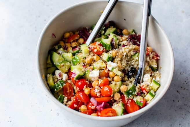 Tossing together veggies with quinoa and dressing in a large bowl.