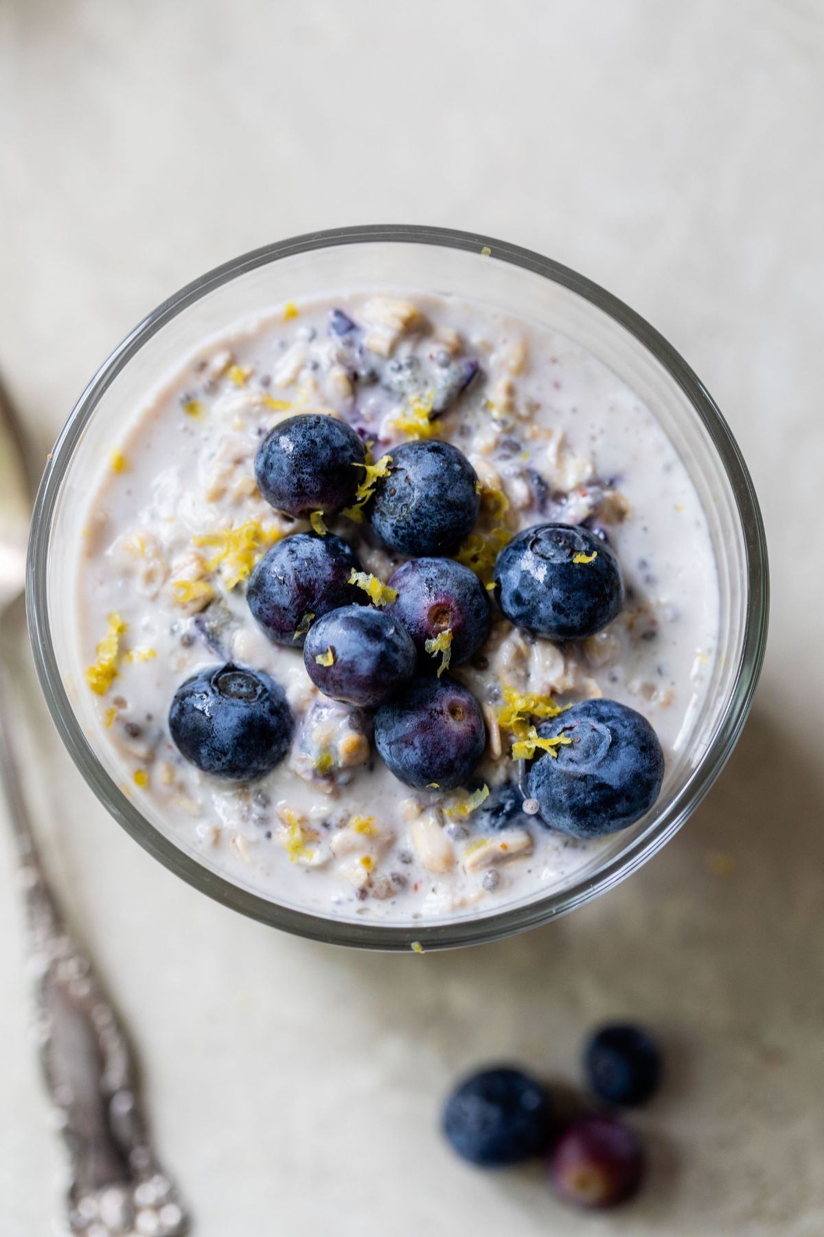Overhead image of overnight oats in a glass topped with blueberries and lemon zest.