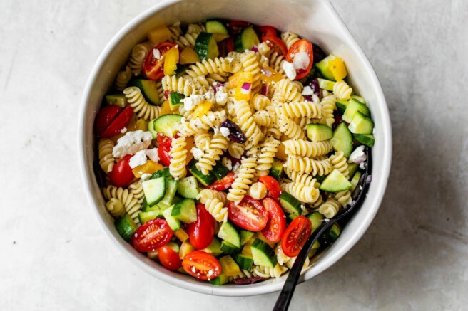 Greek pasta salad topped with dressing in a large bowl.