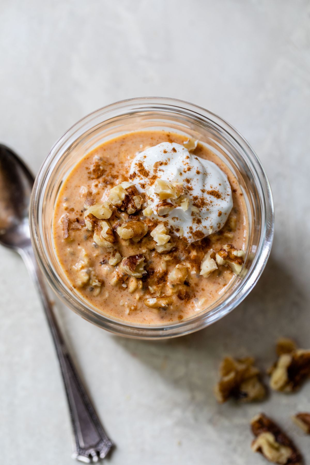 Top view of a jar filled with pumpkin oatmeal and topped with yogurt and walnuts.