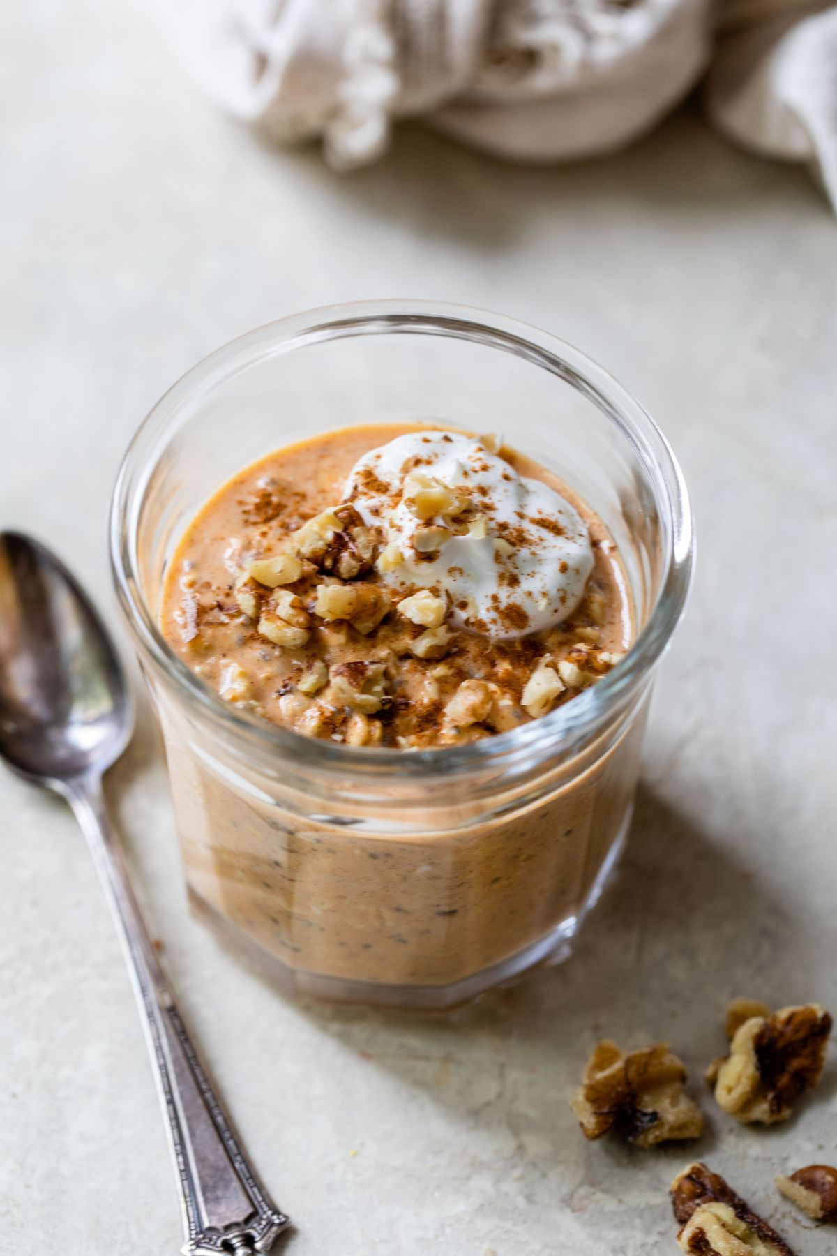 Pumpkin overnight oats in a glass jar topped with nuts and yogurt.