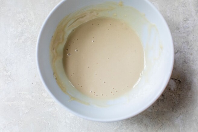Adding water to tahini dressing in a bowl.