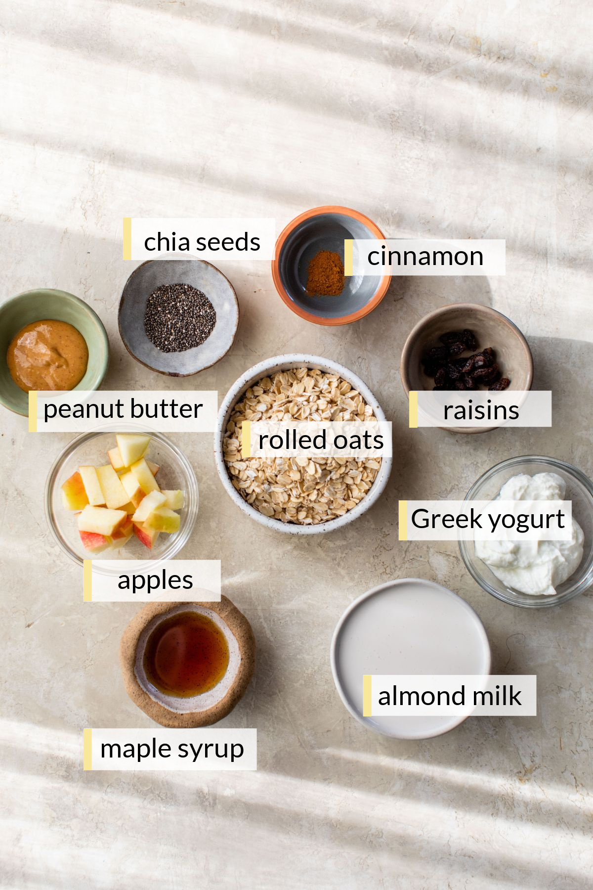 Oats, apples, raisins, Greek yogurt and milk divided into small bowls.
