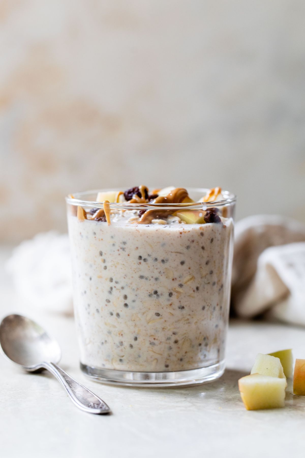 Glass filled with overnight oats and topped with chopped apple, raisins and peanut butter.