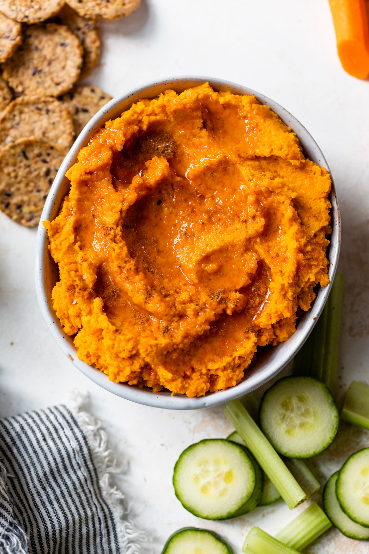 roasted carrot hummus in a small white bowl surrounded by veggies and crackers