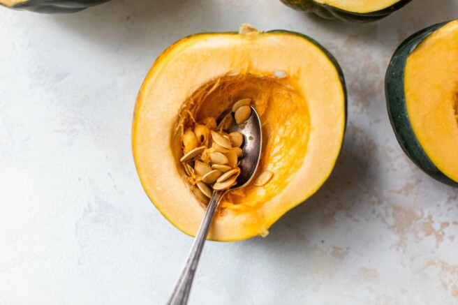 Using a spoon to remove seeds from an acorn squash.
