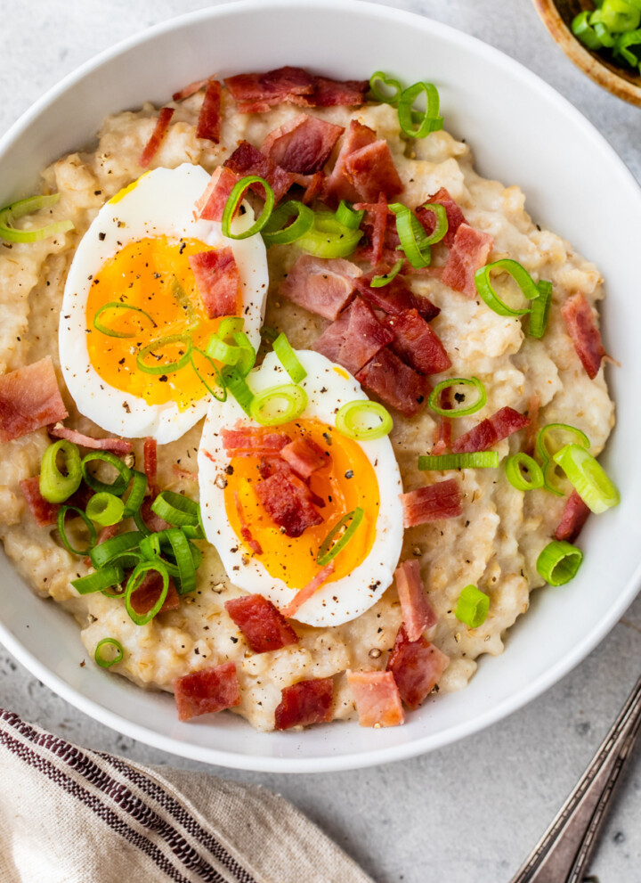 Bowl of savory oats topped with hard boiled egg and turkey bacon