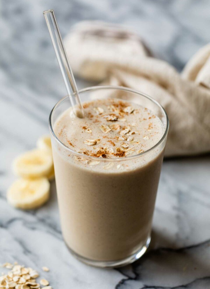 Breakfast smoothie in a glass with a straw garnished with oats and cinnamon.