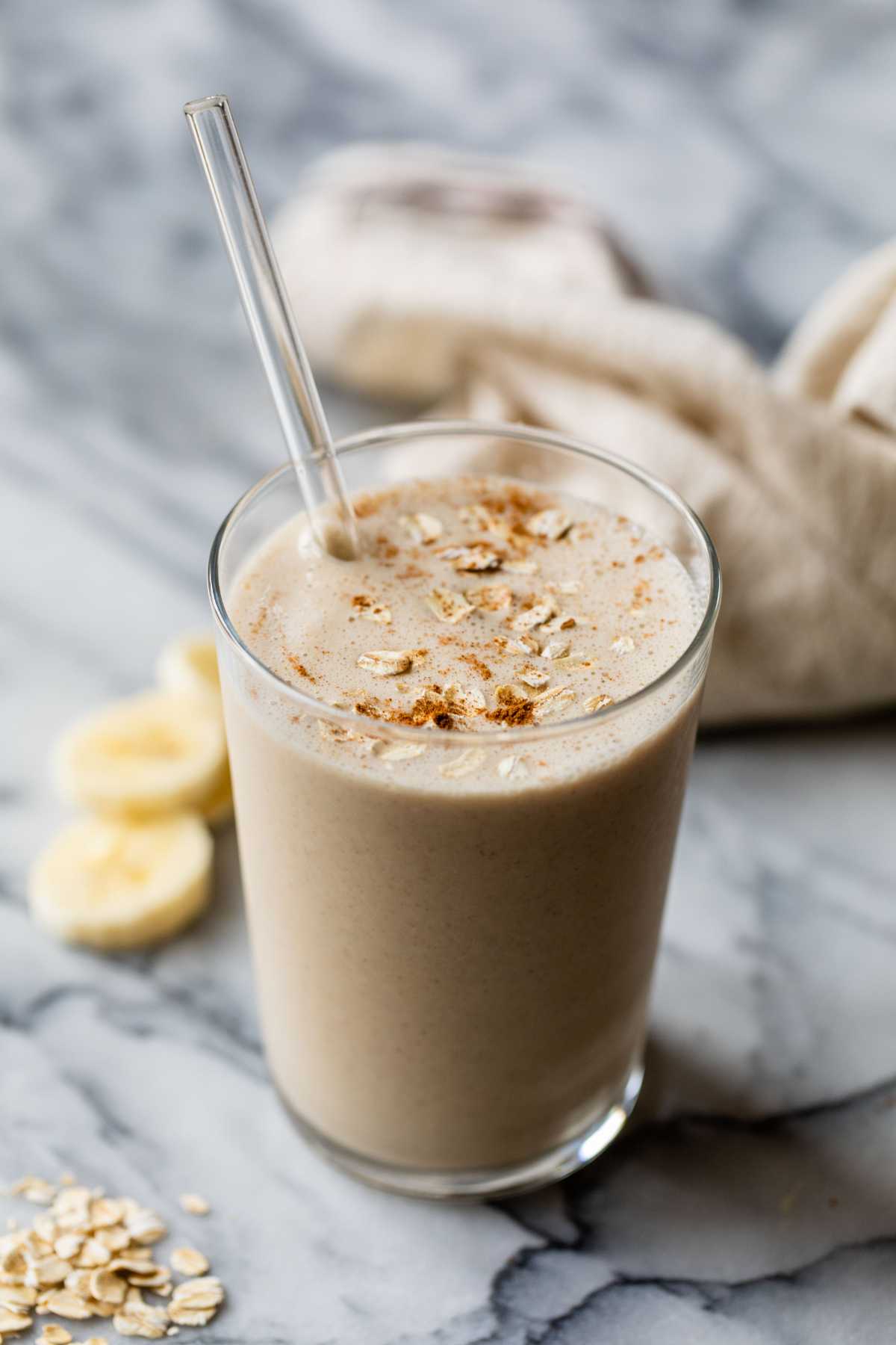 Breakfast smoothie in a glass with a straw garnished with oats and cinnamon.