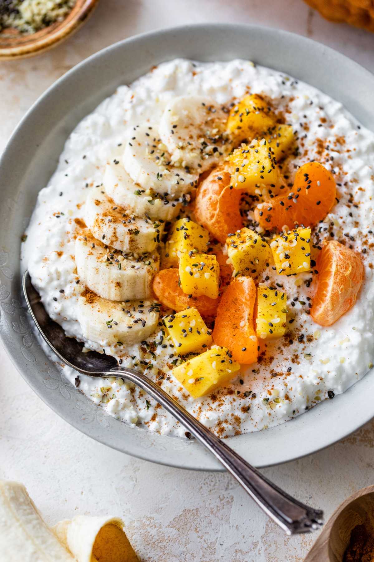 Cottage cheese breakfast bowl topped with banana slices, chopped mango and seeds.