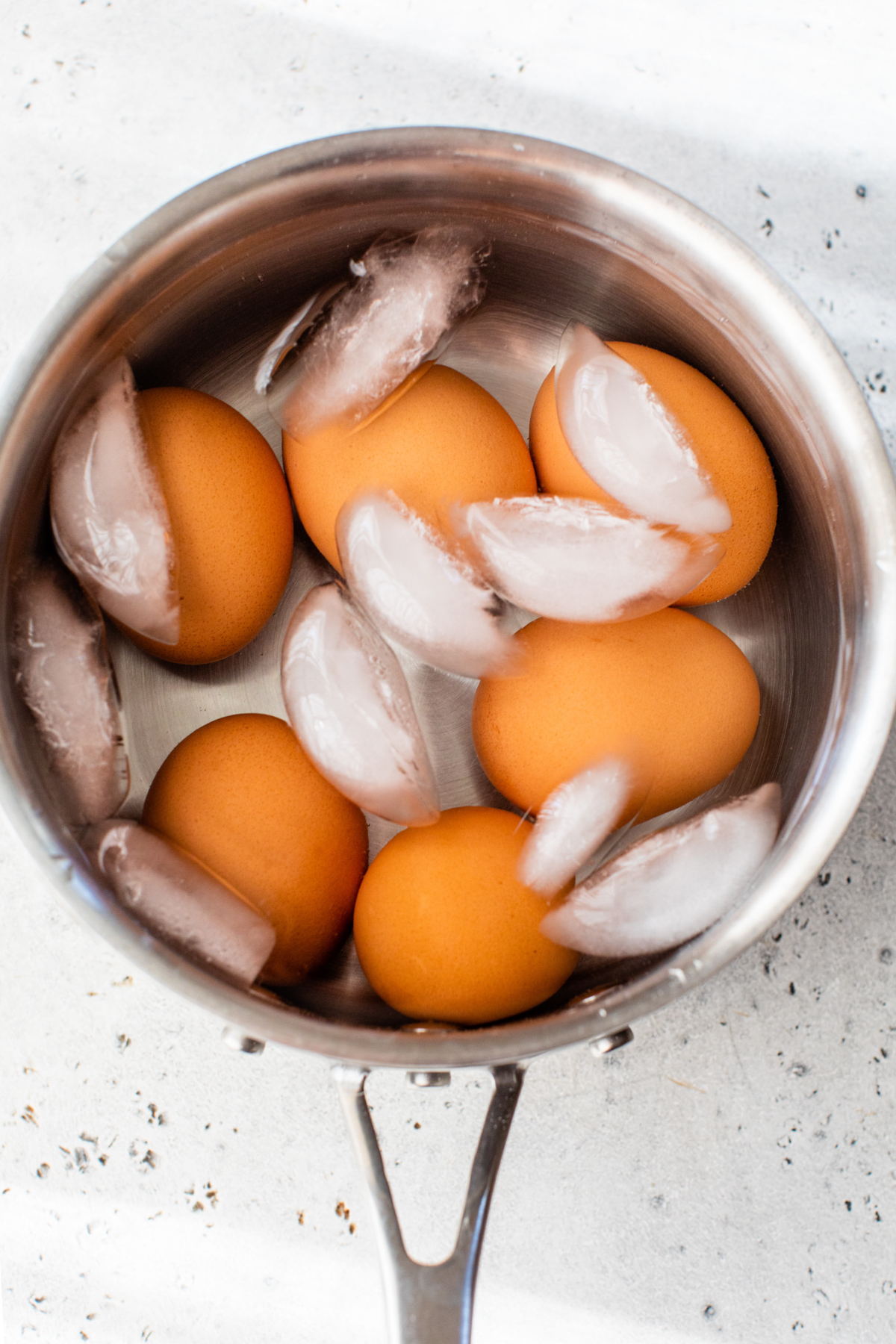 Cold water and ice cubes added to a pot of hard oiled eggs to help them cool