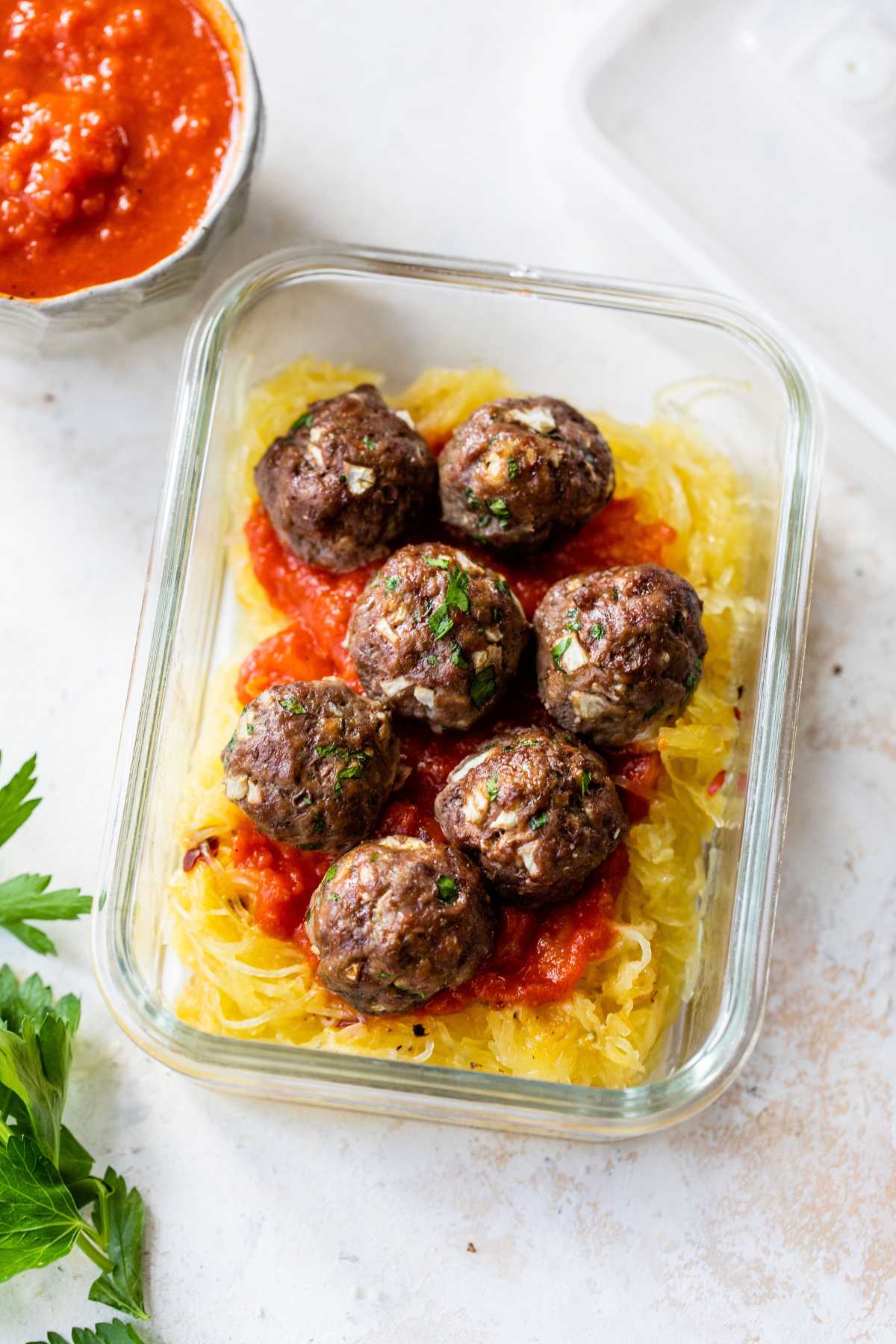 Baked meatballs in a glass container with squash and marinara.