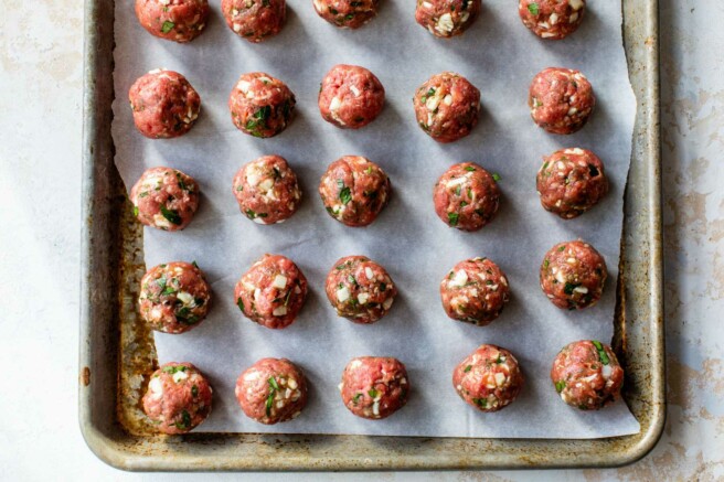 Raw meatballs on a parchment lined pan.