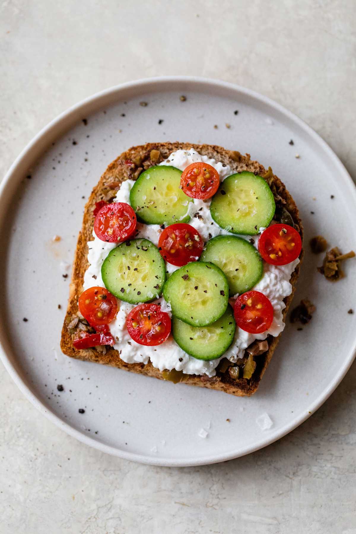 Toast with black olive tapenade, cottage cheese, sliced cucumbers, sliced cherry tomatoes and a sprinkle of salt and black pepper.