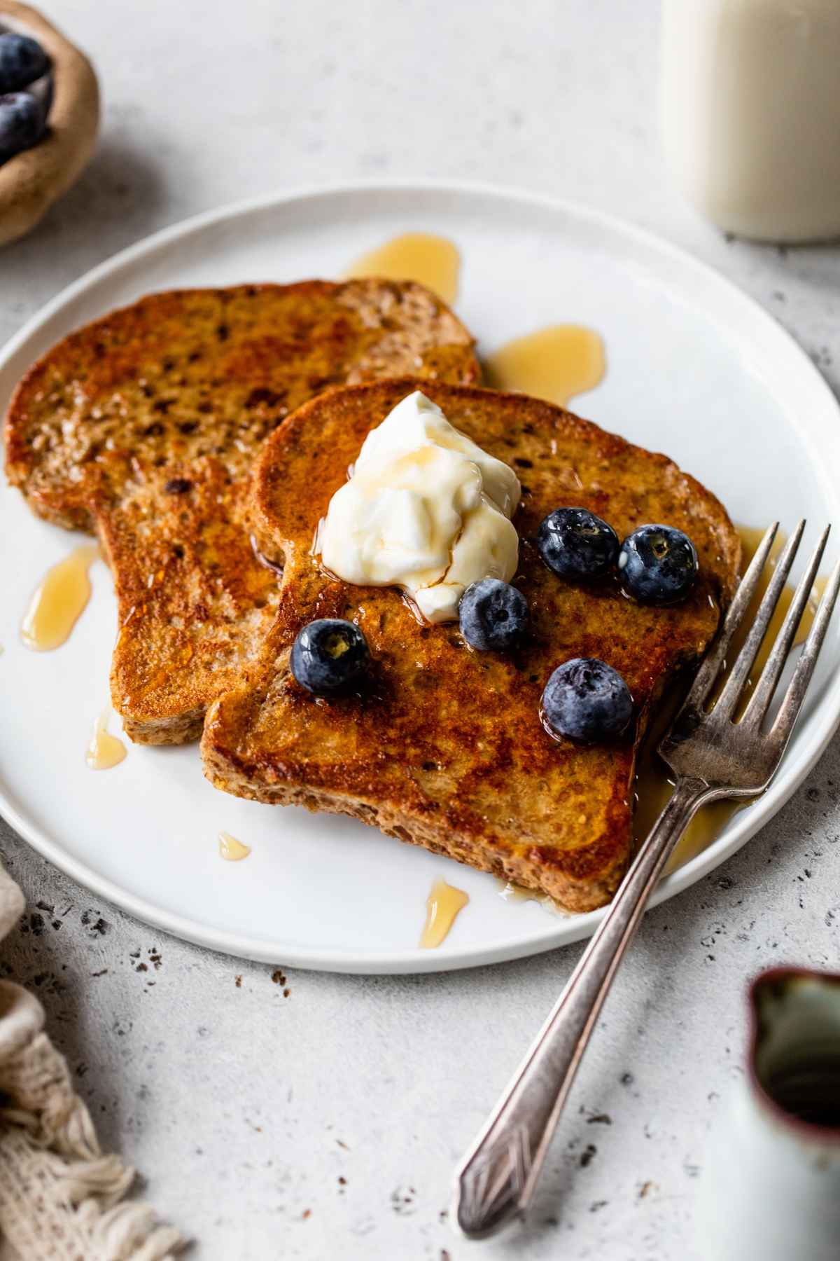 Protein French toast served on a white plate with syrup, fruit and yogurt.