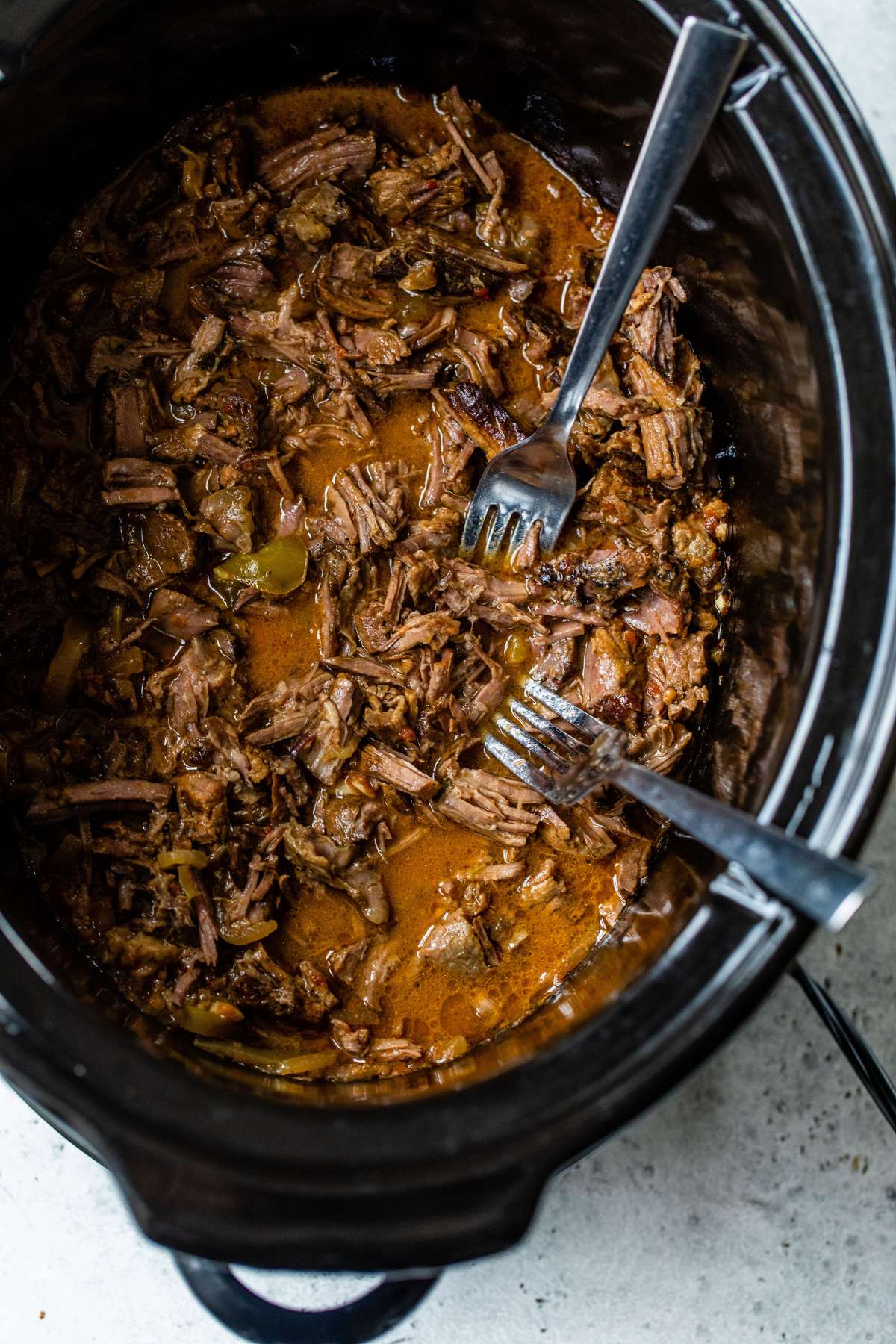 Shredding beef tips with two forks in a slow cooker.