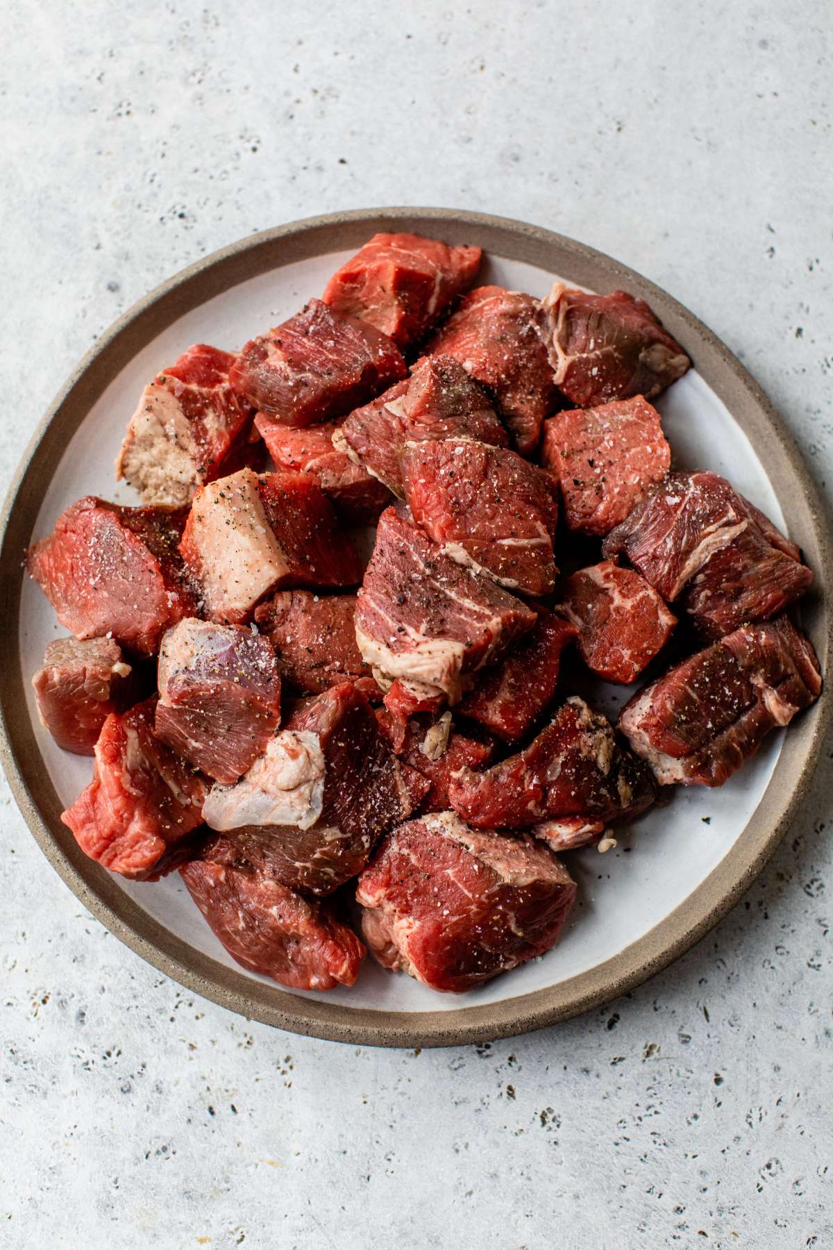 Beef tips on a plate seasoned with salt and pepper.