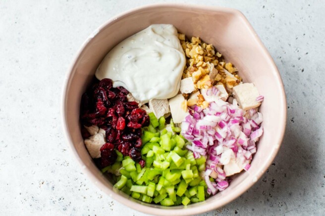 Large bowl with dressing, red onion, celery, cranberries and walnuts.