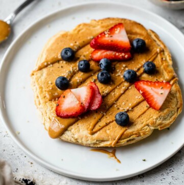 Protein pancake on a white plate with a drizzle of peanut butter and fresh berries.