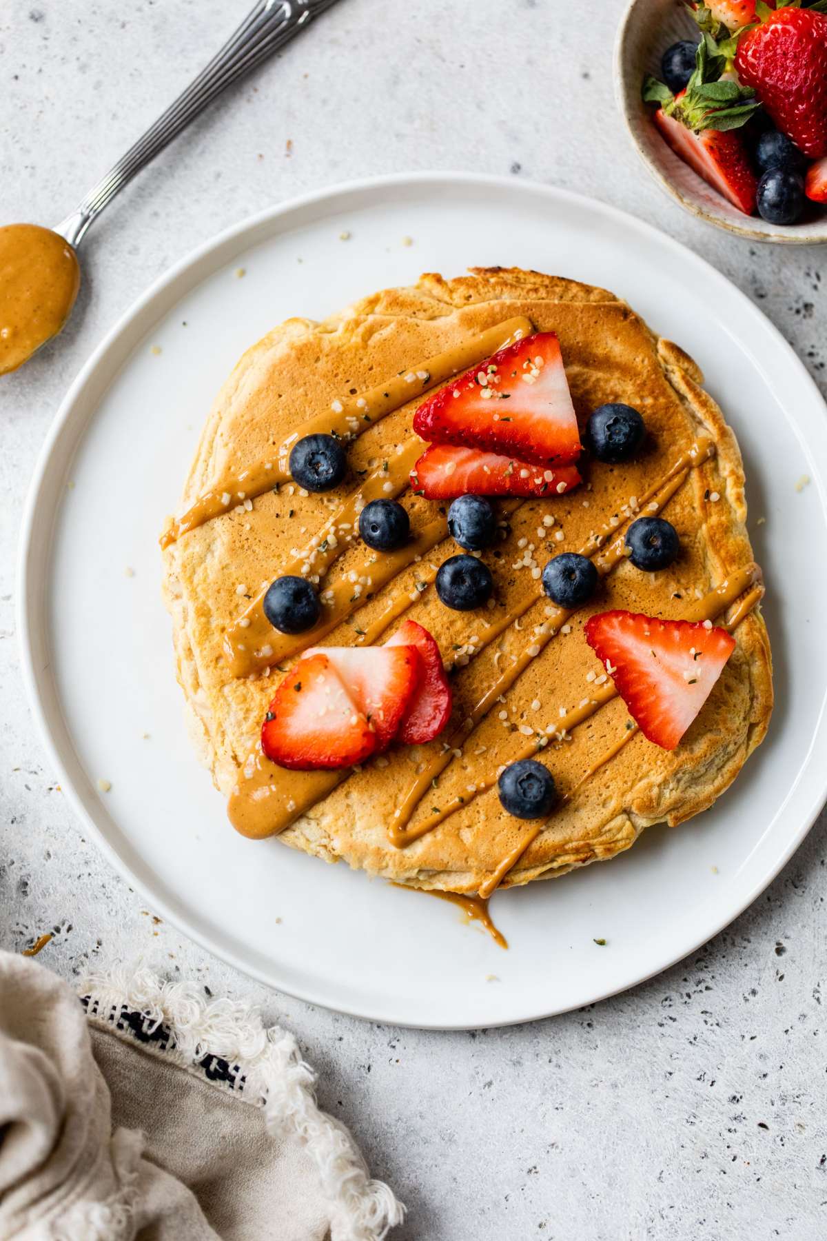 Pancake served on a white plate with peanut butter, strawberries and blueberries.