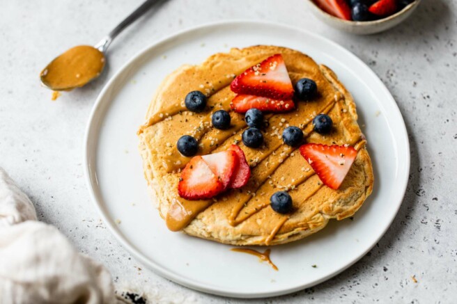 Protein pancake on a white plate with a drizzle of peanut butter and fresh berries.