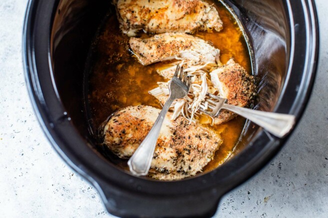 Two forks shredding chicken in a slow cooker.