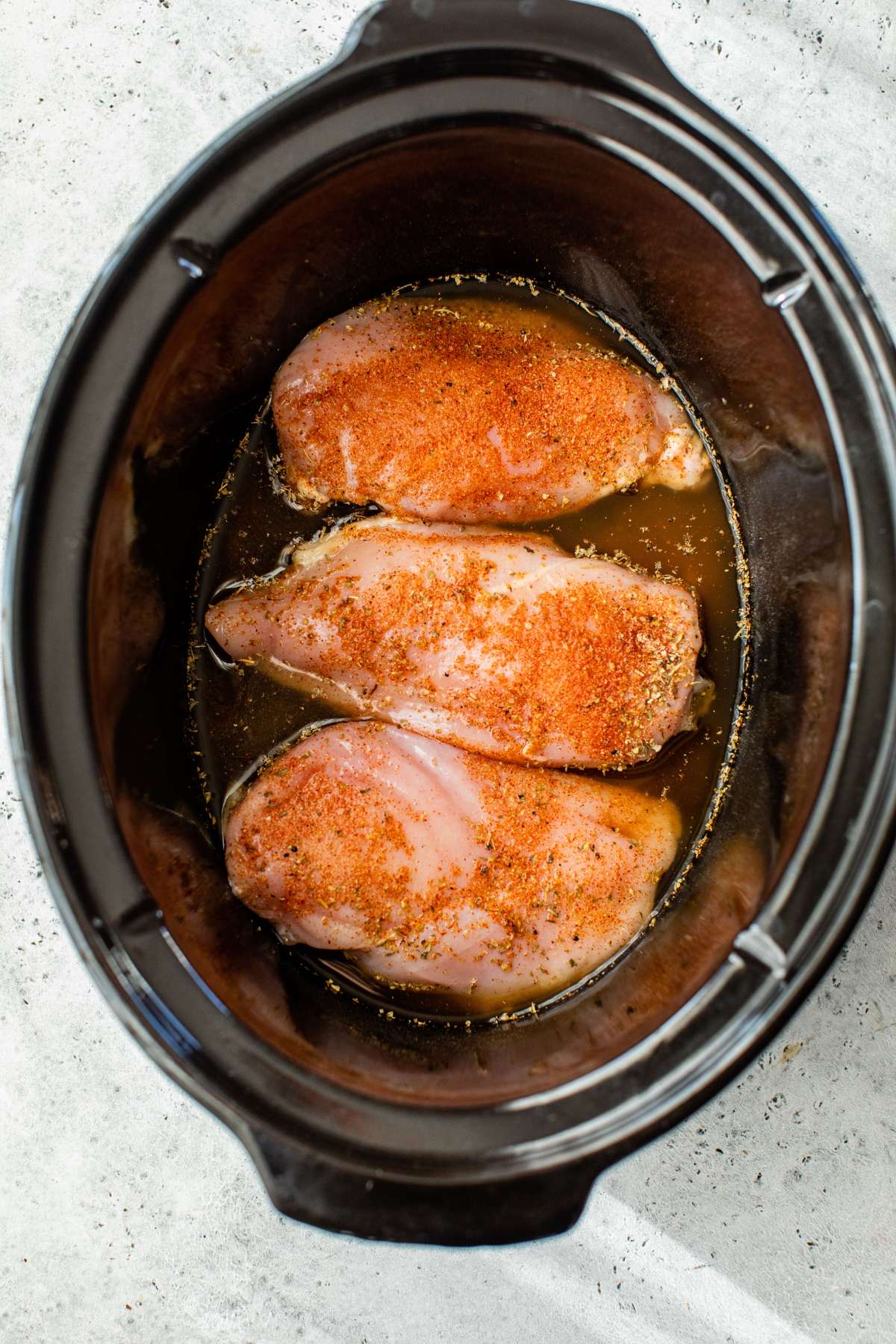 Three chicken breasts with seasoning in a slow cooker.