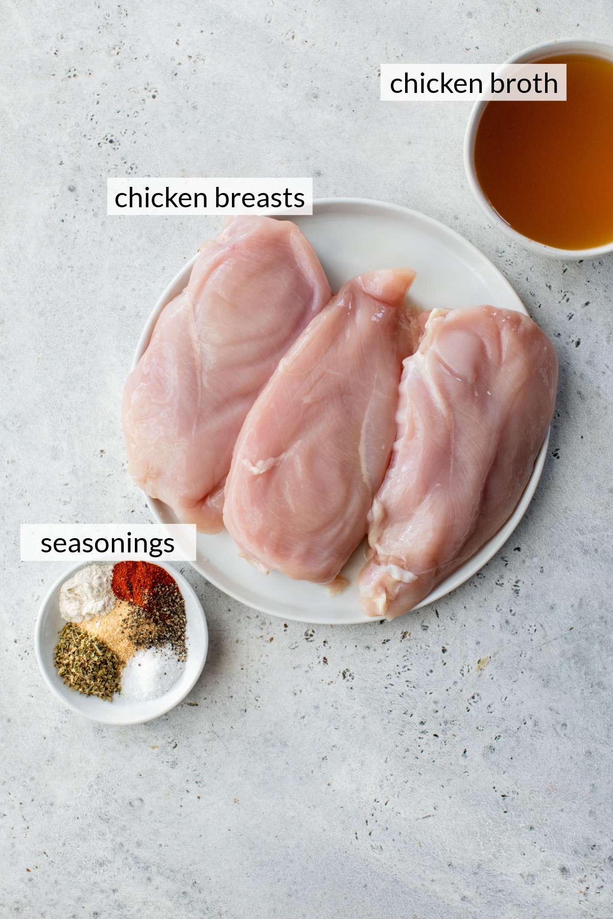 Raw chicken breasts near a bowl of broth and a small plate of spices.
