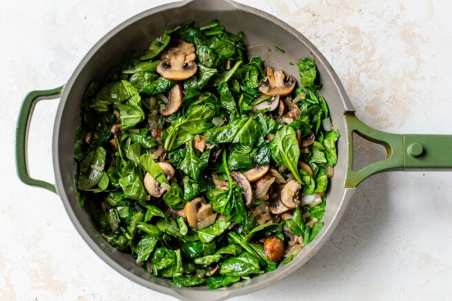 Sautéing spinach with mushrooms in a large skillet.
