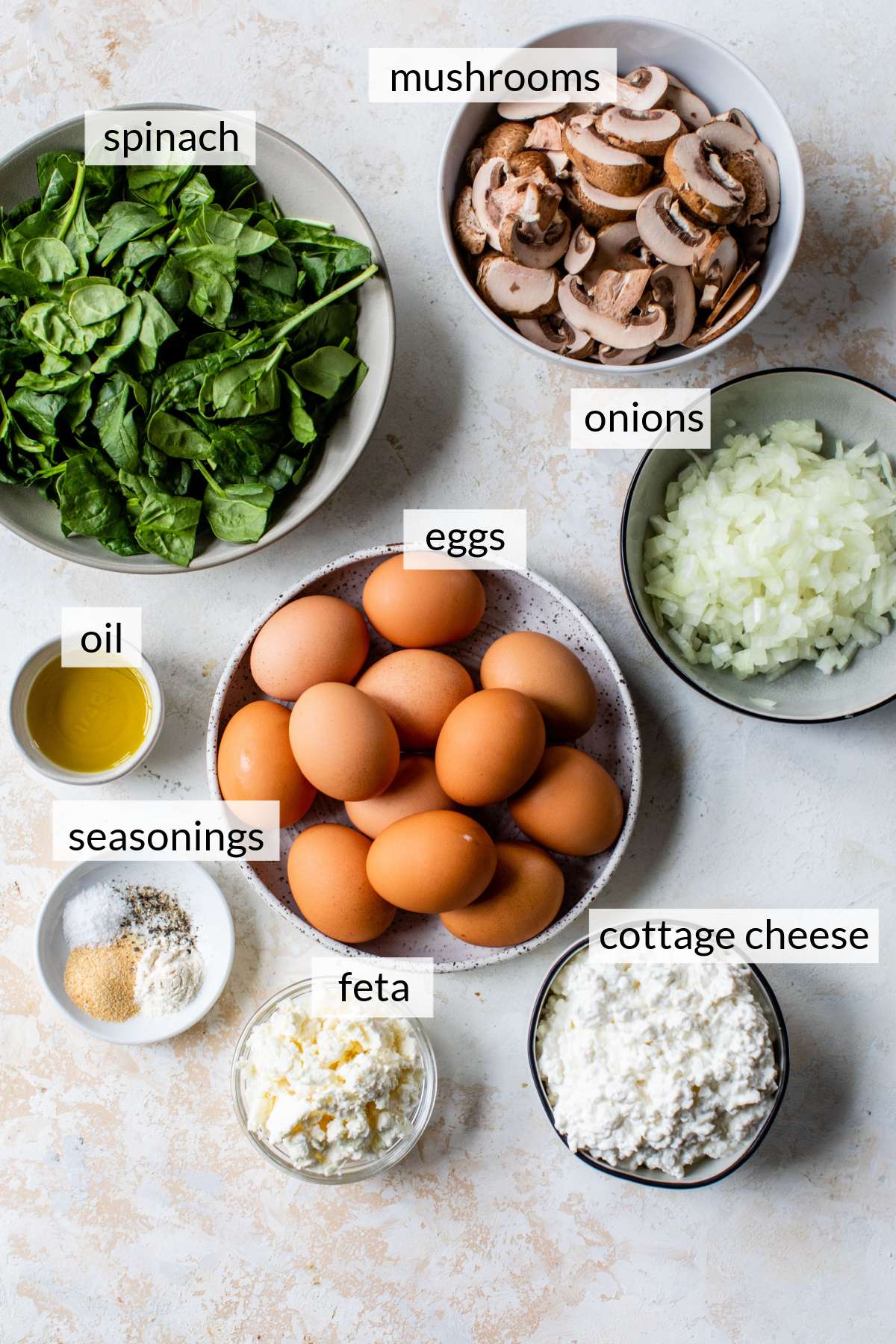 Bowls with eggs, spinach, mushrooms, oil, onions, cottage cheese, feta and seasonings.