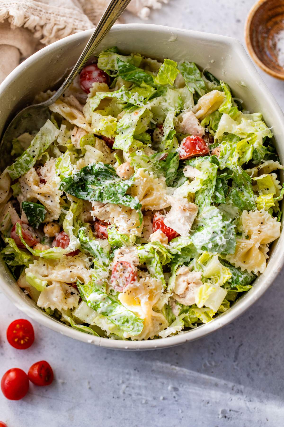 Large bowl filled with romaine lettuce, tomatoes, and bowtie pasta.