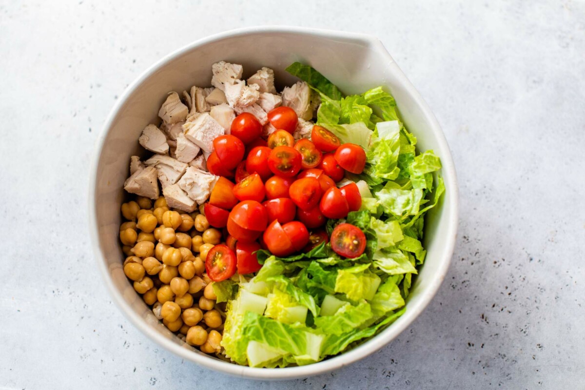 Chickpeas, romaine, tomatoes and chicken added to large bowl.