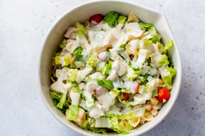 Dressing poured over the top of a salad in a large bowl.