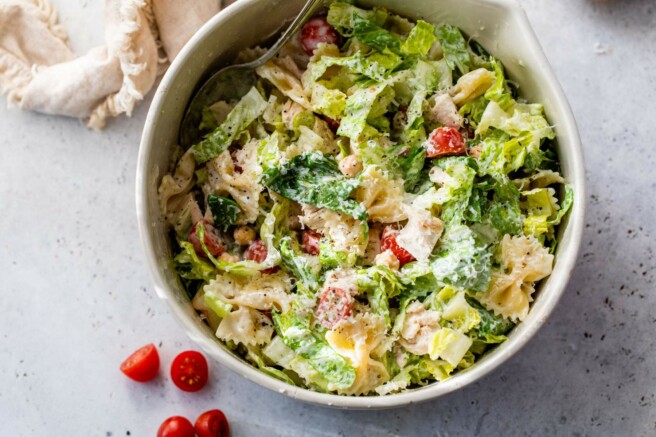 Chicken caesar pasta salad in a large bowl with a serving spoon.