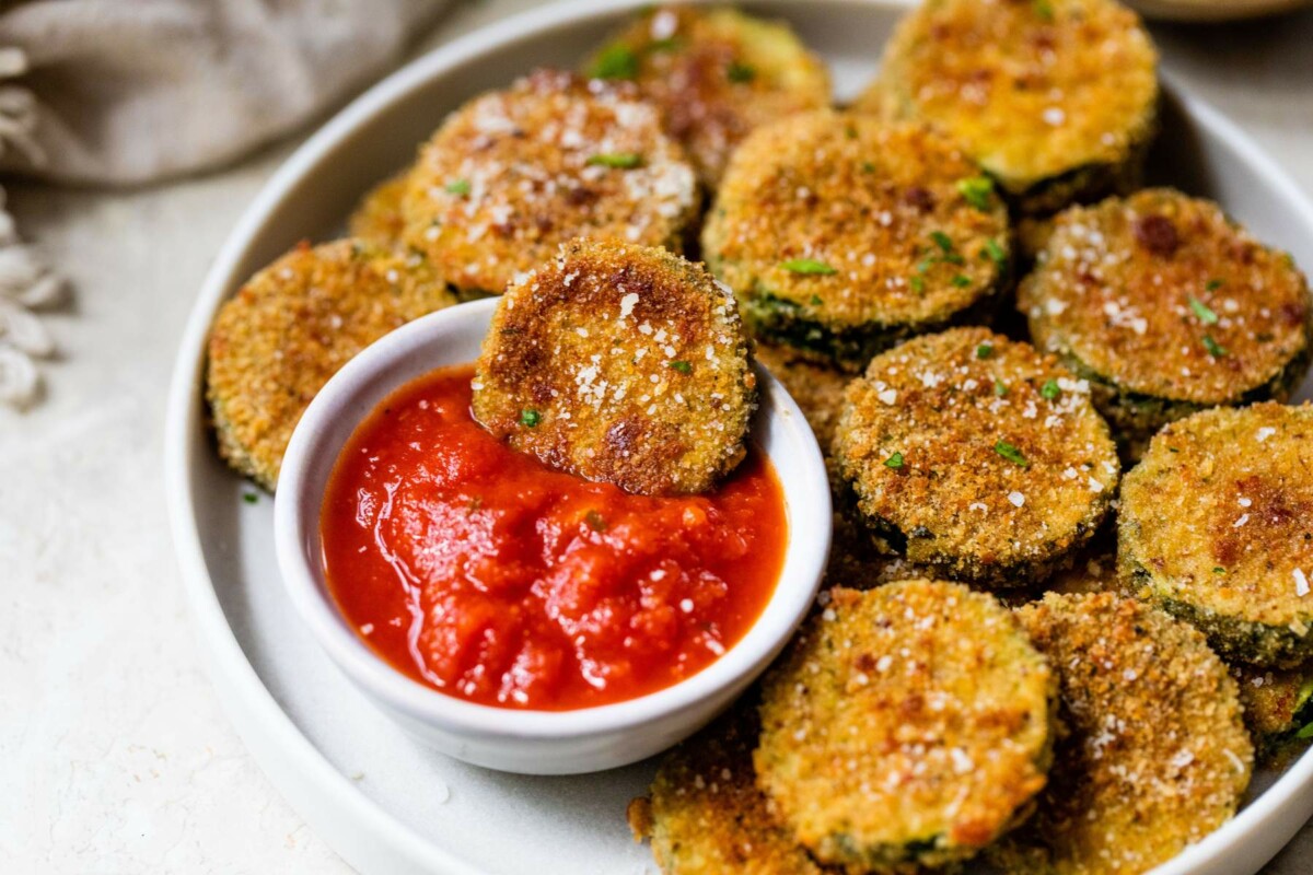 Zucchini chips on a plate with one dipping into marinara.