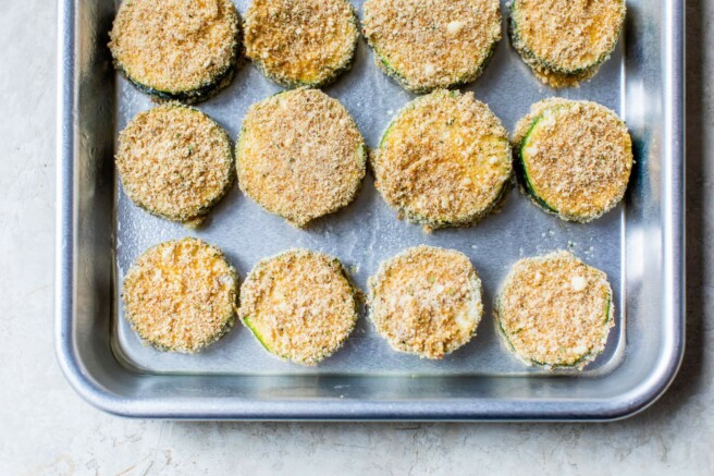 Breaded zucchini slices on a baking sheet pan.