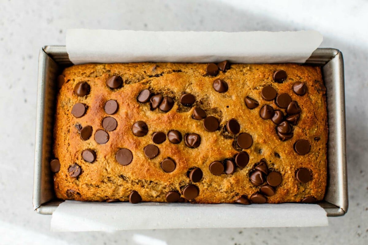 Baked banana bread in a loaf pan lined with parchment paper.